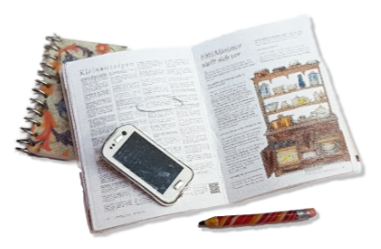 Aufgeschlagene Miniatur-Zeitschrift mit Kleinanzeigen, darauf ein Spiralblock, ein Bleistift und ein Smartphone im Maßstab 1 zu 12